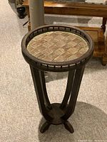 Wooden plant stand with woven top surface, curved legs, and round base shown in detail