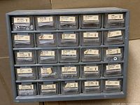 Front view of gray plastic single sided screw caddy showing 24 labeled compartments with screws and hardware supplies.