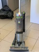 Front view of upright vacuum cleaner showing clear dust canister, branding, and attached hose.