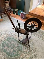 Full side view of antique wooden spinning wheel showing large wheel, foot pedal, and framework.