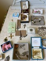 Full view of assorted jewellery laid on table including religious crosses, pins, chains, and small boxes with jewellery inside.