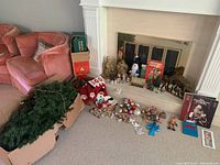 Wide view showing artificial tree parts, Christmas stockings, ornaments, figurines, and books aligned around fireplace and box.