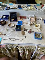 Full view of assorted jewelry items displayed on a vanity surface including brooches, necklace chains, earrings, and small boxes containing jewelry.