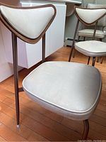 Close-up of chair seat and back showing beige vinyl upholstery with wooden trim and dark brown metal frame