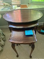Full view of the three wooden nesting tables stacked, showing scalloped oval tops and carved cabriole legs