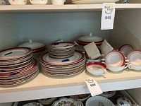 Full view of stacked plates, bowls, and serving dishes with consistent red and gold trim pattern.