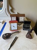 Photo showing four small clocks, wooden mandolin miniature, tuning fork, and small carved wooden seal figurine on countertop.