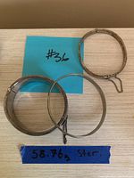 Three sterling silver bangles displayed on a table with blue notes. One is engraved and has a safety chain.