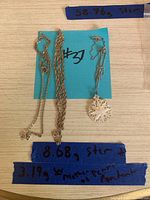 Two sterling silver chains and a mother of pearl pendant on a chain shown on a tabletop with blue tape labels listing weights