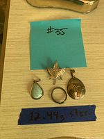 All items displayed: maple leaf pendant, teardrop pendant with blue stone, oval pendant with engraved design, simple silver ring, and handwritten labels.