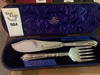 Both utensils displayed in original fitted case with purple lining