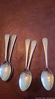 Six sterling silver spoons arranged in groups showing their front side, illustrating their design and polished condition.