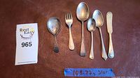 Full view of seven pieces of sterling silver flatware on brown background with weight note