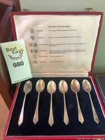 Six sterling silver spoons displayed inside a lined red box with a booklet showing hallmark chart.