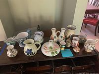 Image showing all 13 ceramic vases and pitchers arranged on a wooden table with various floral and painted designs