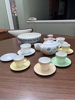 Set of 6 multi-color teacups with saucers, white teapot with blue flower pattern, sugar bowl, creamer, large bowl on table