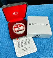 Silver dollar coin displayed in open velvet-lined clamshell case with certificate and outer white box showing Royal Canadian Mint logo.