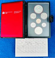 Opened black leather folio with red interior and Royal Canadian Mint logo, displaying the seven coins underneath a plastic protective cover alongside a specification sheet.