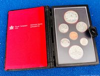 View of original black leather folio with red inner lining and Royal Canadian Mint branding, open to display coins behind clear plastic sheet.