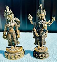 Full front view of two antique Thai bronze Saraswati sculptures with intricate detail and patina showing on bases and figures.