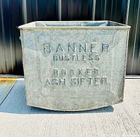 Front view of galvanized tin ash sifter showing 'Banner Dustless Rocker Ash Sifter' debossed lettering on metal surface.