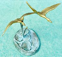 Front elevated view of brass flying geese mounted on bronze base, showing gold color on birds and detailed base surface.