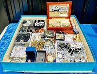 Overhead view of turquoise tray showing wooden jewelry box and clear storage boxes filled with necklaces, bracelets, earrings and pendants
