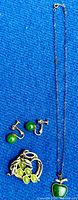 Photo showing all jewelry pieces arranged on blue fabric: necklace with jade apple pendant, brooch with jade accents, and screw back earrings with round jade stones.