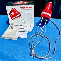 Photo showing the KitchenAid Ultra Power hand mixer with stainless steel turbo beaters attached, along with its power cord, user manuals, and original box on a blue surface.