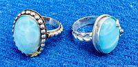 Two sterling silver rings with blue and white oval Larimar stones on blue fabric background.