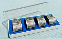Set of four pewter napkin rings displayed in white box with blue velvet lining and clear lid.