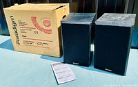 Pair of Paradigm loudspeakers with original box and instruction manual displayed on table.