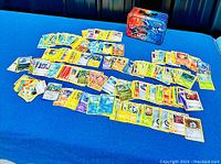 Wide view image showing numerous Pokémon cards spread out on a surface along with a metal storage tin featuring Pokémon artwork.