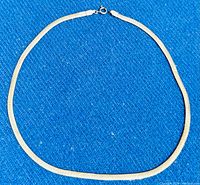 Full view of a flat, wide sterling silver herringbone chain necklace with spring ring clasp on a blue textured background.
