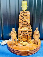 Full view of the hand carved folk art lamp showing the fireplace base, figures, and lamp socket on top.