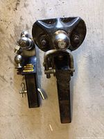 Photo showing two tow hitches with ball mounts and hitch pins, placed side by side on concrete floor.