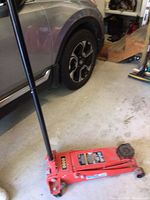 Side view of red floor jack with handle placed upright near vehicle wheel