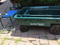 Side view of green Ames Planters Wagon made of resin plastic with four large black wheels and green handle features including grips.