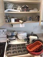 Kitchen shelves with baking tools including mixing bowls, hand mixer, baking pans, measuring cups and various kitchen utensils.