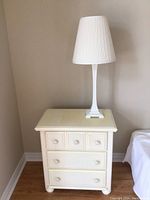 Front view of white distressed bedside table with white lamp on top.