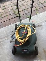 Front view of the green Black & Decker electric lawn mower with yellow extension cord coiled on top. Shows overall condition and model label.