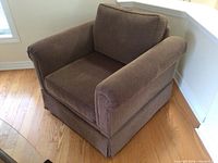 Front-left angled view of the brown oversized chair showing rolled arm, seat and back cushions, and skirted base.