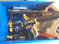 Top view of blue plastic box containing yellow and black Quick-Grip clamps and hand saws with wooden handles.