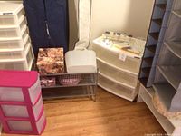 Full view of closet organizer items including pink and white plastic drawers, cardboard boxes, small basket, shoe trays, clothes covers and fabric shelves.