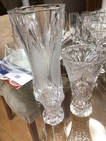Three crystal vases of different sizes and patterns arranged on a glass table with reflections, no chips or cracks visible