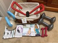 Exercise weights including 2 five-pound dumbbells, 2 one-pound dumbbells, 2 kettlebells with blue handles, a Thigh Master with red padded grips, DVDs for meditation and kettlebell workouts, Fitbit Inspire HR and a wicker basket with cotton liner.
