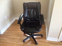 Front view of black faux leather swivel desk chair with armrests on wooden floor.
