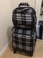 Full view of the large suitcase and the small toiletry bag stacked on top, showing black plaid pattern and structure.