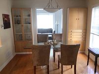 Two IKEA cabinets positioned in a dining room with a glass dining table and upholstered chairs. One cabinet with glass doors, the other solid wood doors with drawers.