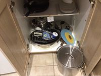 View inside cupboard showing various pots, pans, racks, and lids including large stock pot and smaller pans